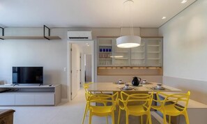 Cozinha moderna com área de jantar, televisão de tela plana e cadeiras amarelas.