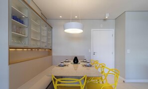 A modern dining area with a round table, yellow chairs, and a hanging light fixture. - Apart Near the Beach in Cond. w/ Pool Adc0205 (Florianópolis)
