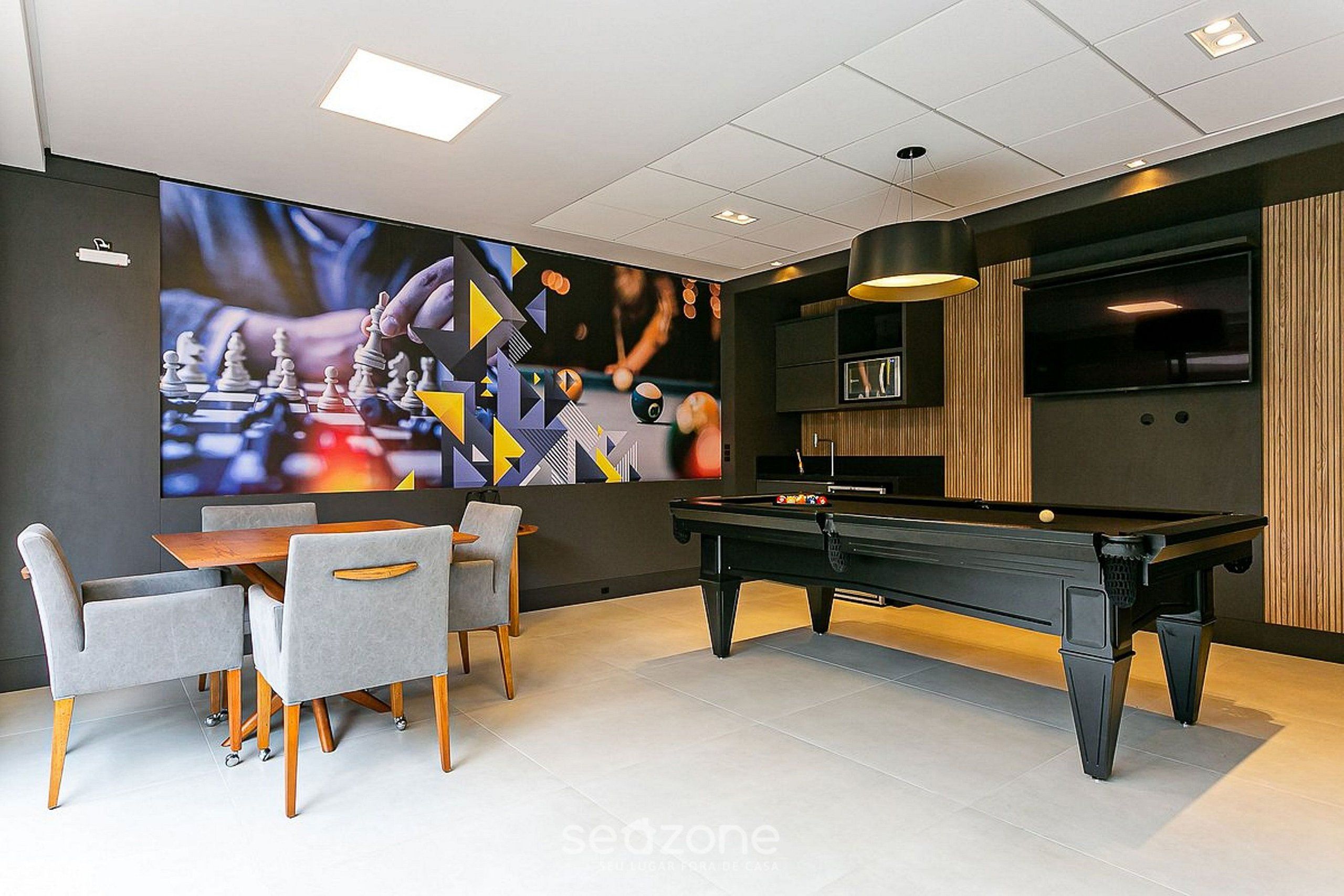 Une pièce moderne équipée d’une table de billard, de sièges confortables et d’un grand écran diffusant une partie d’échecs.