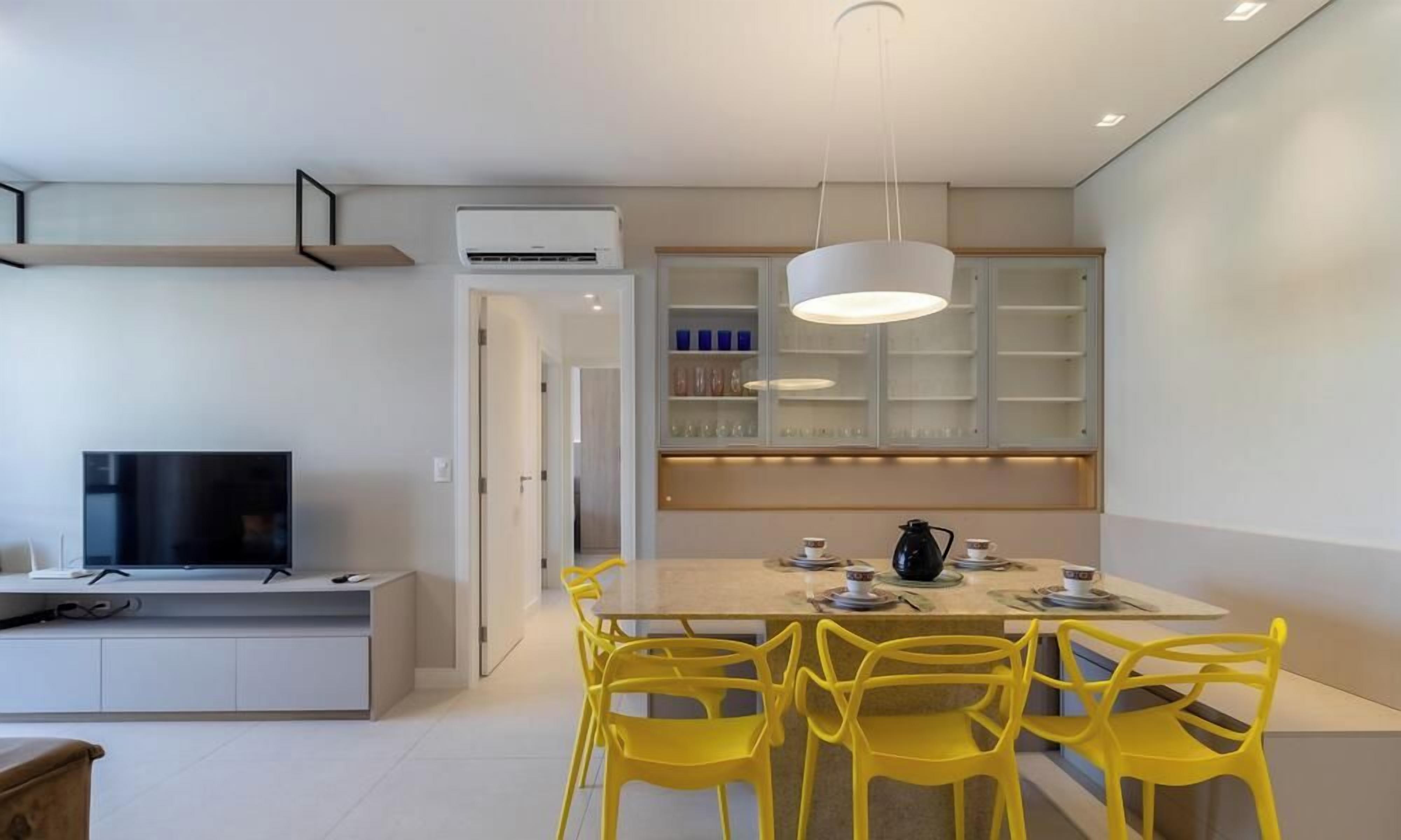 A modern kitchen with a dining area, a built-in TV, and a bright pendant light.