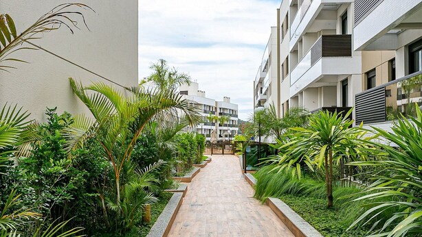 A narrow pathway flanked by lush greenery and modern buildings with balconies. - Apart Near the Beach in Cond. w/ Pool Adc0205 (Florianópolis)