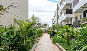 A narrow pathway flanked by lush greenery and modern buildings with balconies. - Apart Near the Beach in Cond. w/ Pool Adc0205 (Florianópolis)