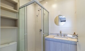 Uma casa de banho moderna com chuveiro em cabine de vidro, toucador com lavatório e espelho, e estantes embutidas.
