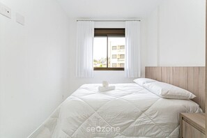 Un dormitorio minimalista con una cama grande, cabecera de madera y una ventana con cortinas blancas.