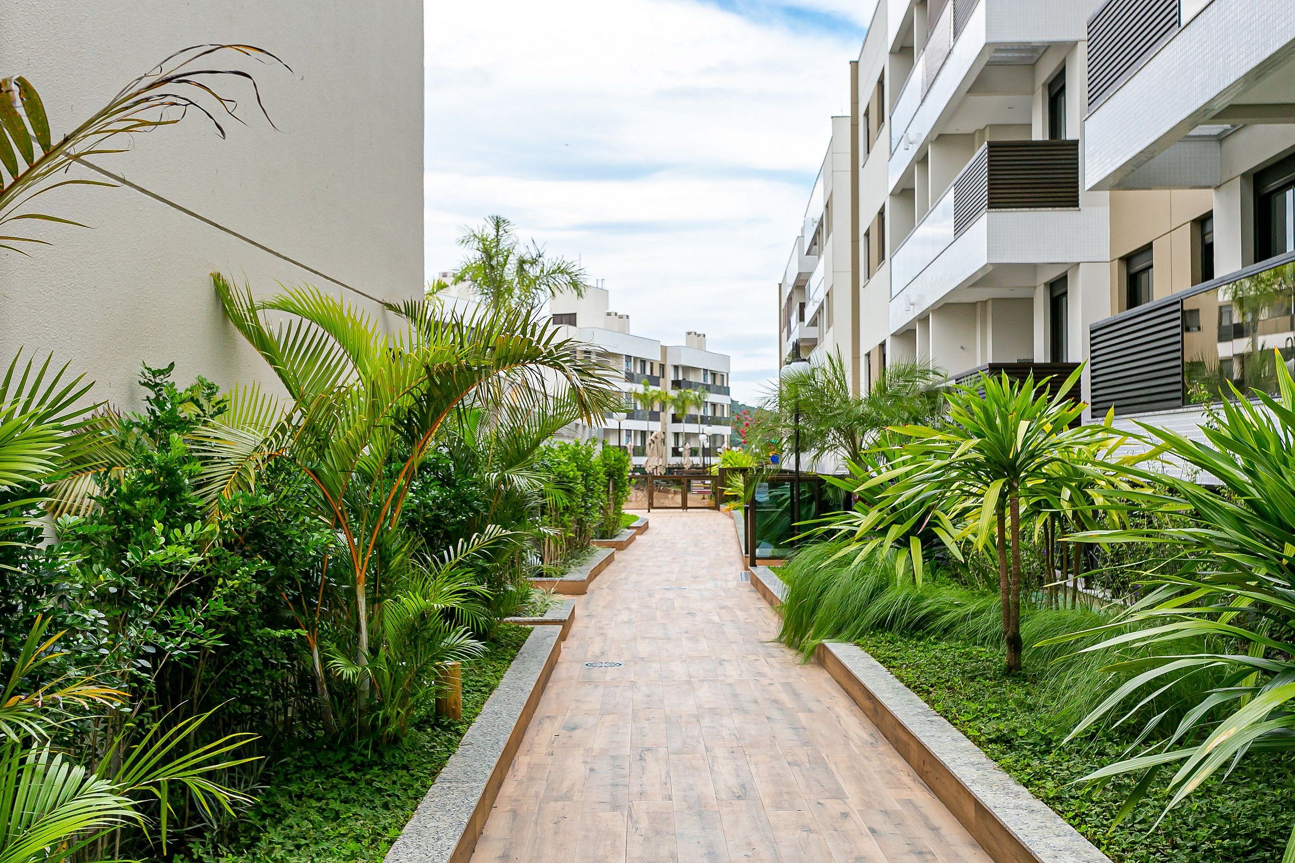 Un sendero bordeado por abundante vegetación y edificios modernos.