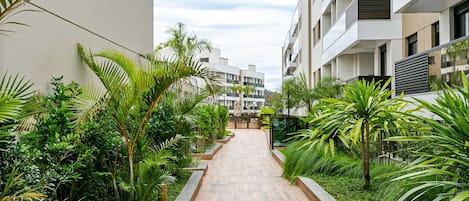 A pathway flanked by lush greenery and modern buildings.