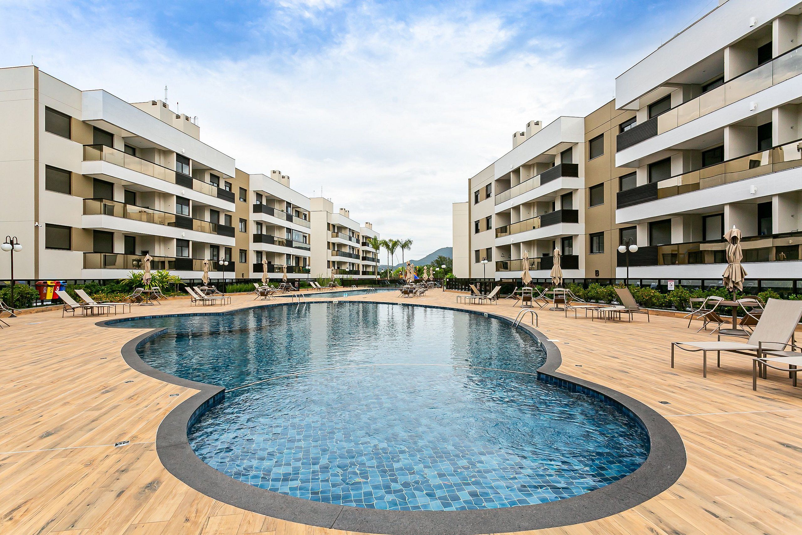 A swimming pool surrounded by lounge chairs and a modern apartment building.