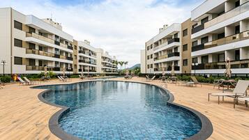 Piscina cercada por espreguiçadeiras e um edifício moderno.