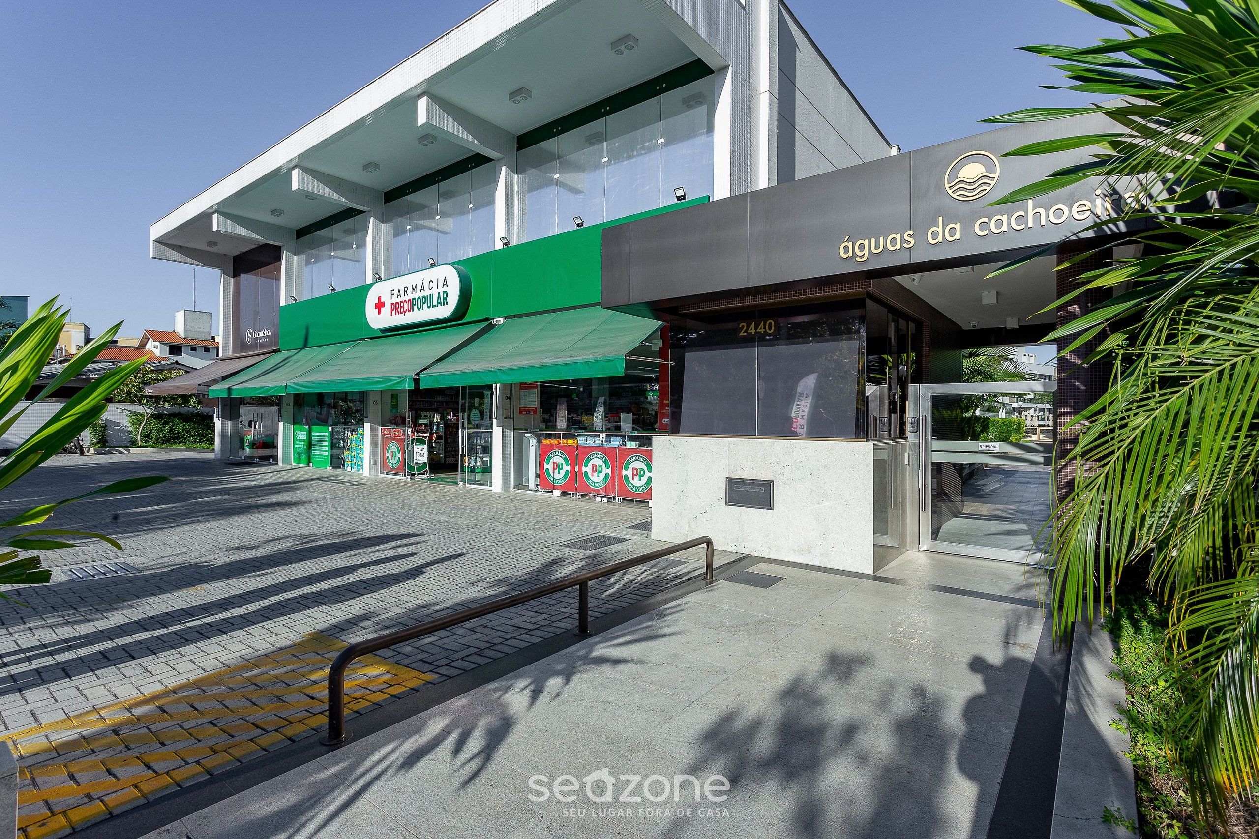 Um edifício moderno com toldo verde e uma placa que diz 'FARMÁCIA PRECOPULAR'.
