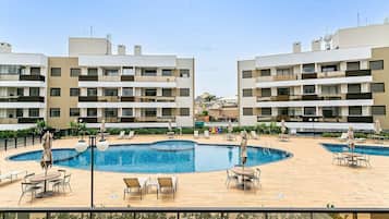 A modern hotel with a central swimming pool surrounded by lounge areas and outdoor seating.