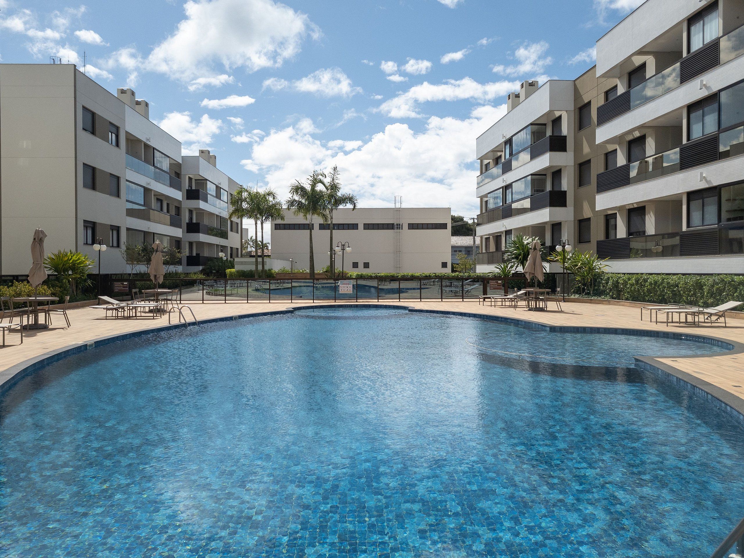 A modern hotel with a central swimming pool, multiple balconies, and outdoor seating areas.