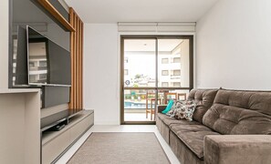 Una sala de estar moderna con una televisión de pantalla plana, un sofá y un puerta corrediza de vidrio que da a un balcón con piscina.