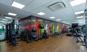 Een sportschool met diverse fitnessapparaten, een houten vloer en een kleurrijke muurschildering.