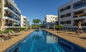 Zwembad met ligbedden en parasols, omringd door moderne appartementencomplexen.