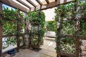 Een overdekt terras met een houten pergola, stenen zuilen en een betonnen vloer.