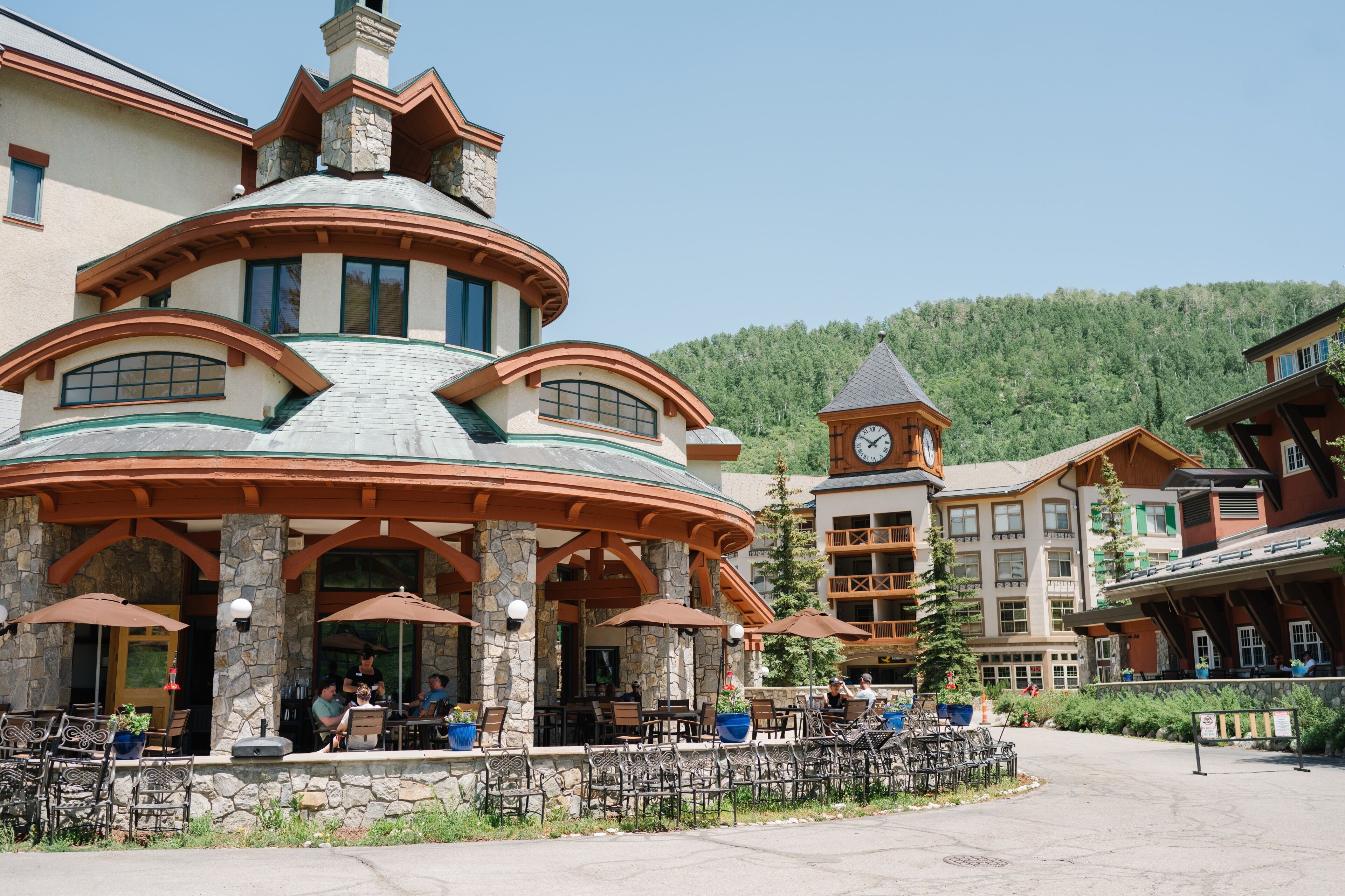 Un bâtiment à la façade en pierre, doté d’une tour horloge et d’une terrasse avec des parasols.