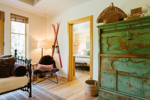 A cozy room with a wooden floor, a green dresser, a chair with a fur throw, and a window with blinds.