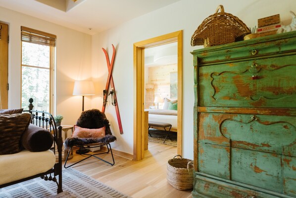 Um quarto aconchegante com piso de madeira, cômoda verde, cadeira com manta de pele e janela com persianas.