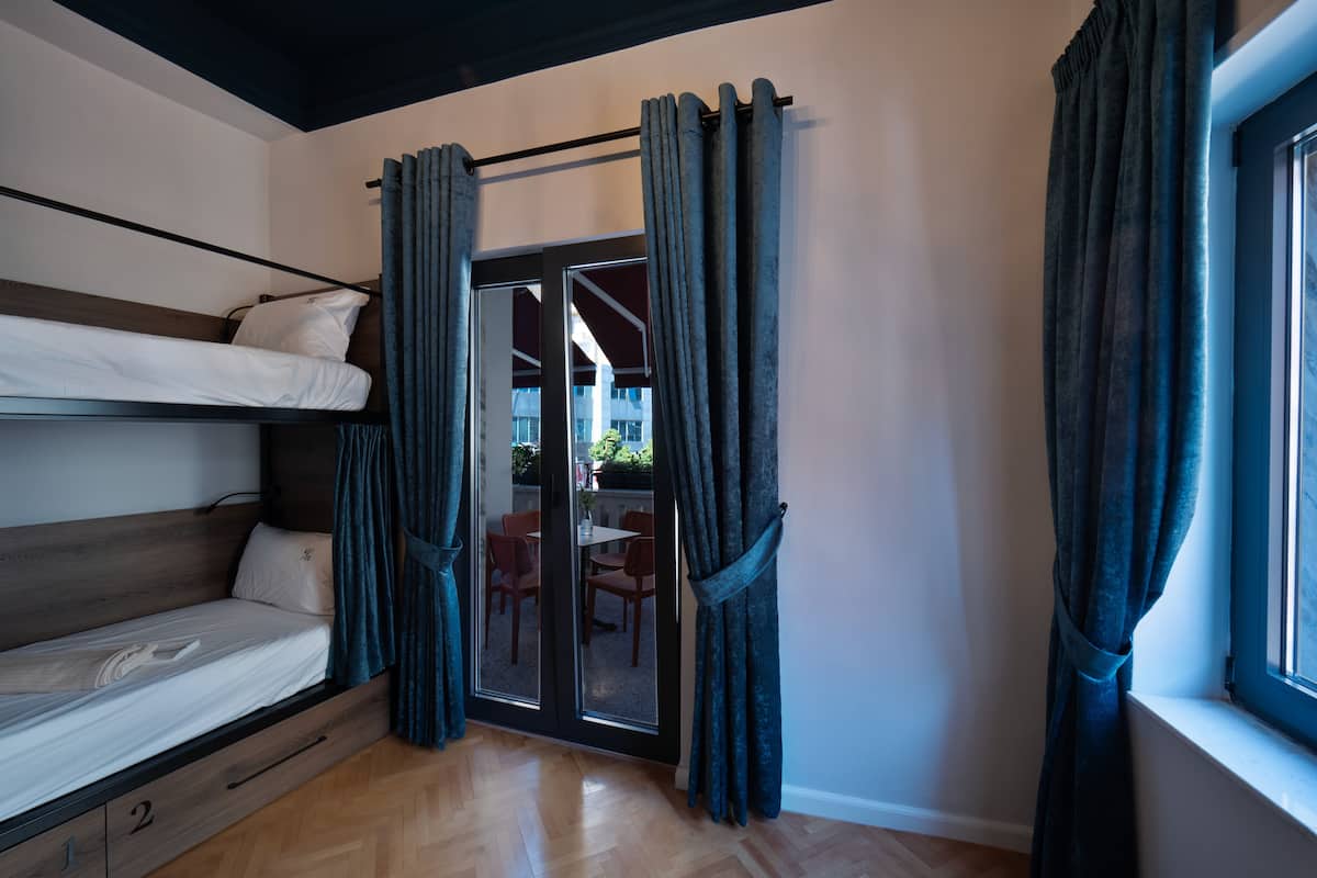 A compact room with a bunk bed, a sliding glass door leading to an outdoor area, and a window with curtains.