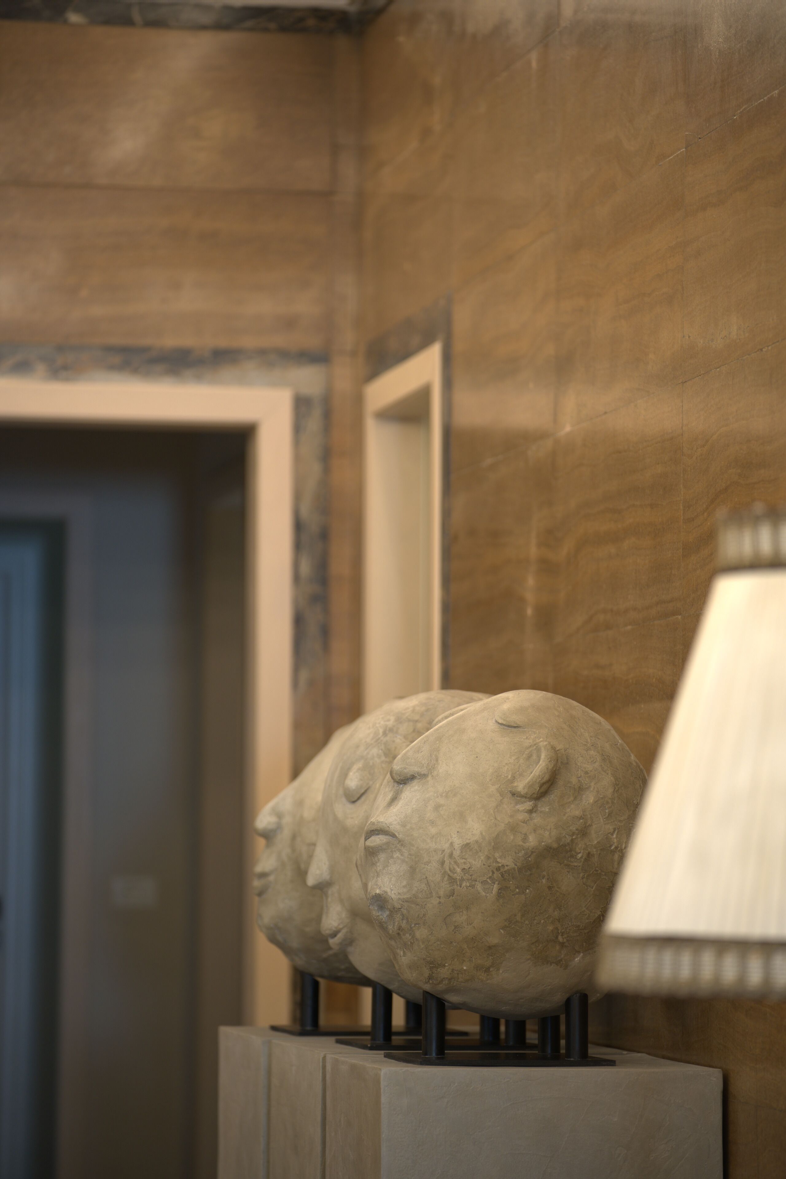 A stone sculpture of a face on a pedestal in a room with wooden paneling and a lamp.