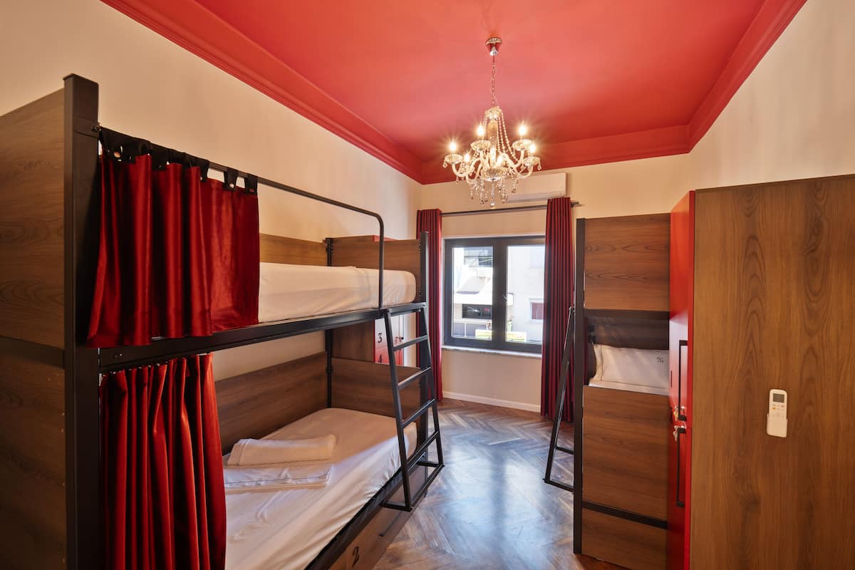 A bunk bed room with a chandelier, wooden walls, and a window with curtains.