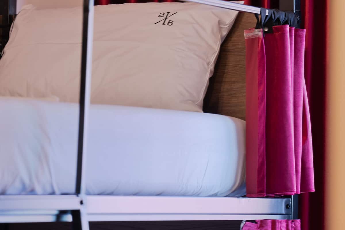 A bed with a metal frame, a white pillow, and a red curtain.