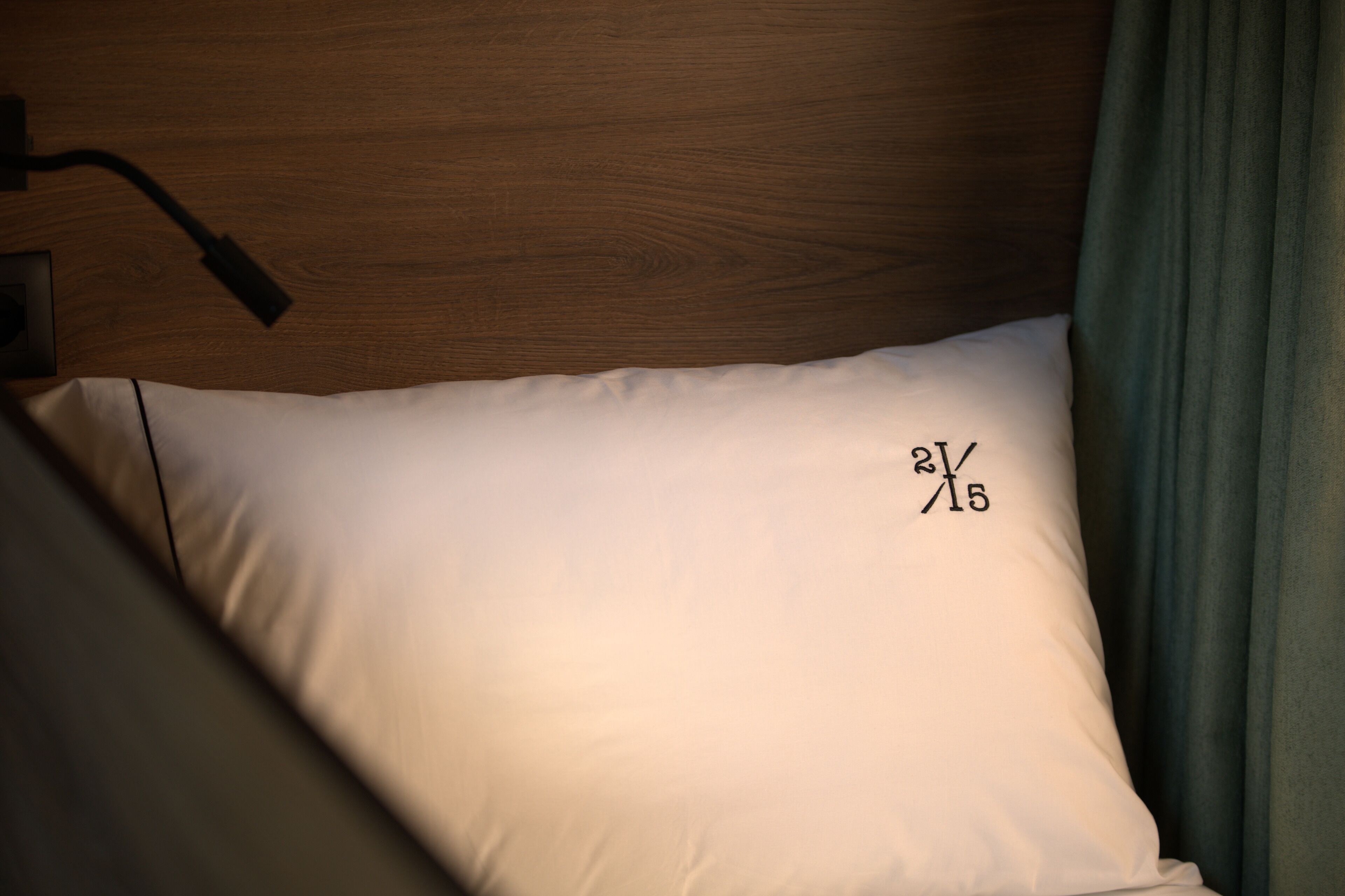 A bed with a white pillow featuring a date '2/15' and a wooden headboard.