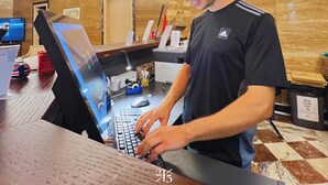A man working at a desk with a computer, a desk lamp, and various office supplies. - 2115 Boutique Hostel (Durrës)