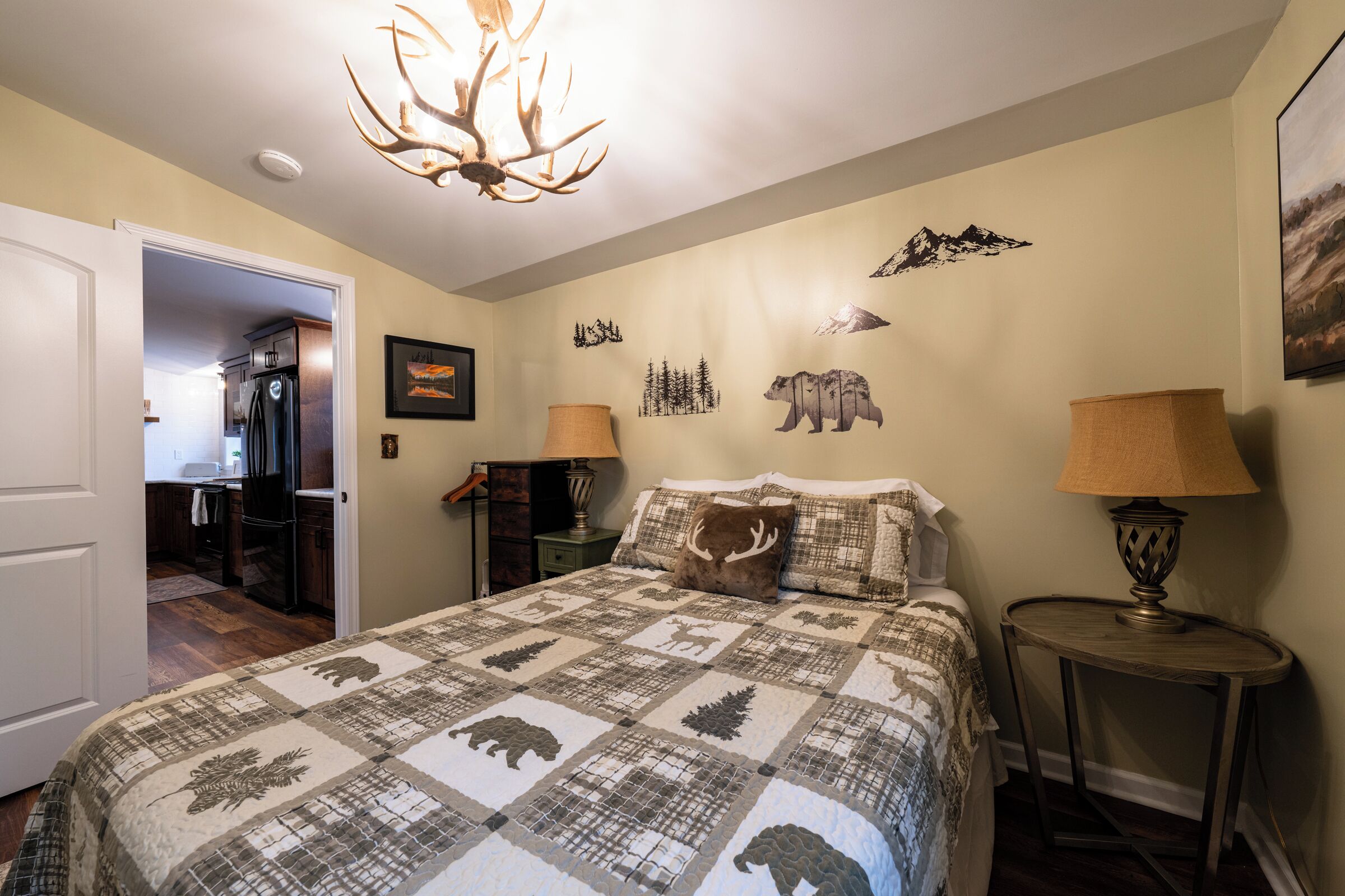 A bedroom with a large bed, a chandelier, a wall with animal decals, and a door leading to a kitchen.