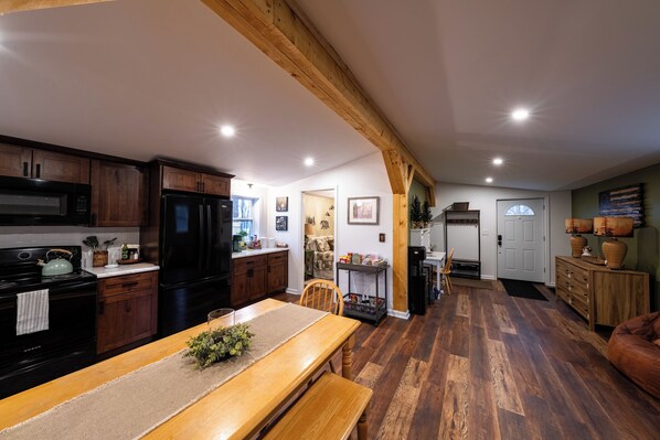 A kitchen with wooden cabinets, a dining table with a bench, and a living area with a sofa. - Cozy Fall Getaway- 35 Min to Bills Stadium- Wineries + Trails (Silver Creek)