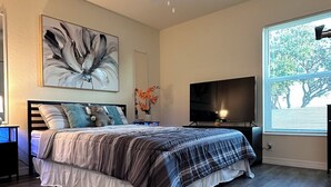 Camera da letto con un letto, una ventola a soffitto, una TV e una finestra con tende.
