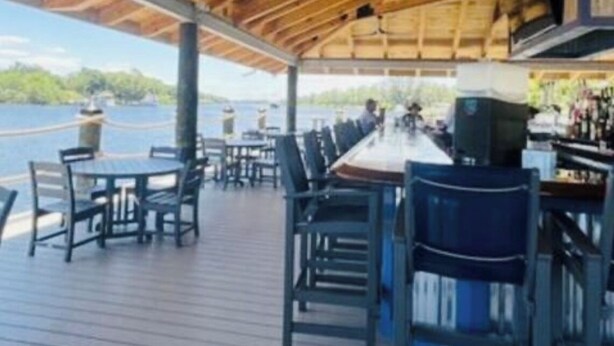 Una terrazza esterna coperta con pavimento in legno, tavoli e sedie, con vista su un corpo d'acqua.