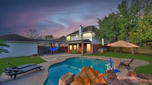 A backyard with a swimming pool, lounge chairs, a hammock, and a patio area with a view of a lake. - Hickory Trl King Bed w/ Pool | Near Jersey Village (Houston)