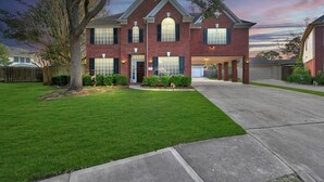 A two-story brick house with a front garage, a well-maintained lawn, and a tree in the front yard. - Hickory Trl King Bed w/ Pool | Near Jersey Village (Houston)