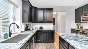 A modern kitchen with dark cabinetry, a marble countertop, and a built-in oven. - Hickory Trl King Bed w/ Pool | Near Jersey Village (Houston)