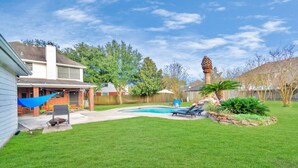 A backyard with a swimming pool, a hammock, and a stone planter. - Hickory Trl King Bed w/ Pool | Near Jersey Village (Houston)