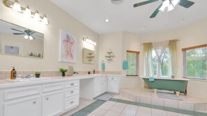 A spacious bathroom with a large vanity, a freestanding bathtub, and a ceiling fan.