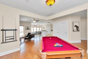 Un grand espace de vie comprenant une table de billard, un ventilateur de plafond et, au fond, un coin repas.