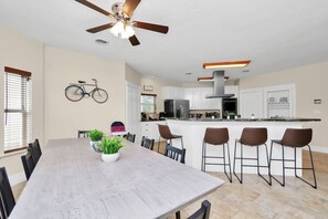 Une cuisine moderne avec des meubles blancs, un îlot central doté de tabourets de bar et un ventilateur de plafond.
