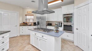 A modern kitchen with white cabinetry, a central island, a stainless steel range hood, and built-in appliances including a microwave and oven.