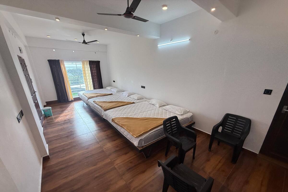 A hotel room with three beds, a ceiling fan, a desk with two chairs, and a window with curtains.