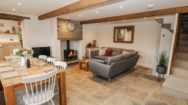 A cozy living room with a stone fireplace, a sofa, and a dining area with a table set for a meal. - Hill Top Cottage (Holmfirth)