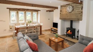 A spacious living room with a stone fireplace, a dining area with a view, and a cozy seating area. - Hill Top Cottage (Holmfirth)