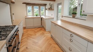 A modern kitchen with wooden flooring, built-in cabinets, a gas stove, and large windows providing natural light. - Hill Top Cottage (Holmfirth)