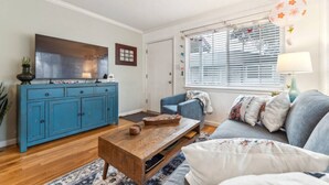 Una sala de estar con un aparador azul, una mesa de centro de madera, un sofá azul y una ventana con persianas.
