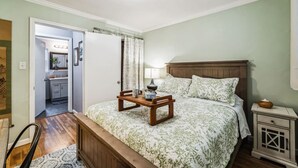 Un dormitorio con cama, mesita de noche, lámpara y una pequeña mesa con tazas y tetera.