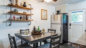 Una cocina con una mesa de comedor, sillas, un refrigerador y estantes con adornos.