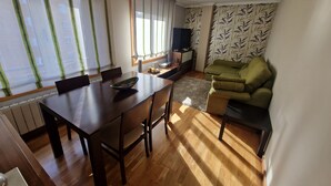 Uma sala de estar com uma mesa de jantar de madeira, um sofá verde e uma televisão.