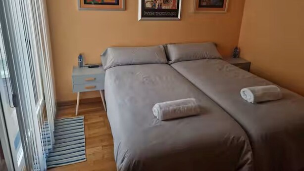 Quarto com uma cama de casal, uma mesinha de cabeceira, uma pequena mesa e duas imagens penduradas na parede.