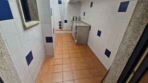 Um corredor estreito com paredes azulejadas em tons de branco e azul, chão de azulejos e uma janela à esquerda.